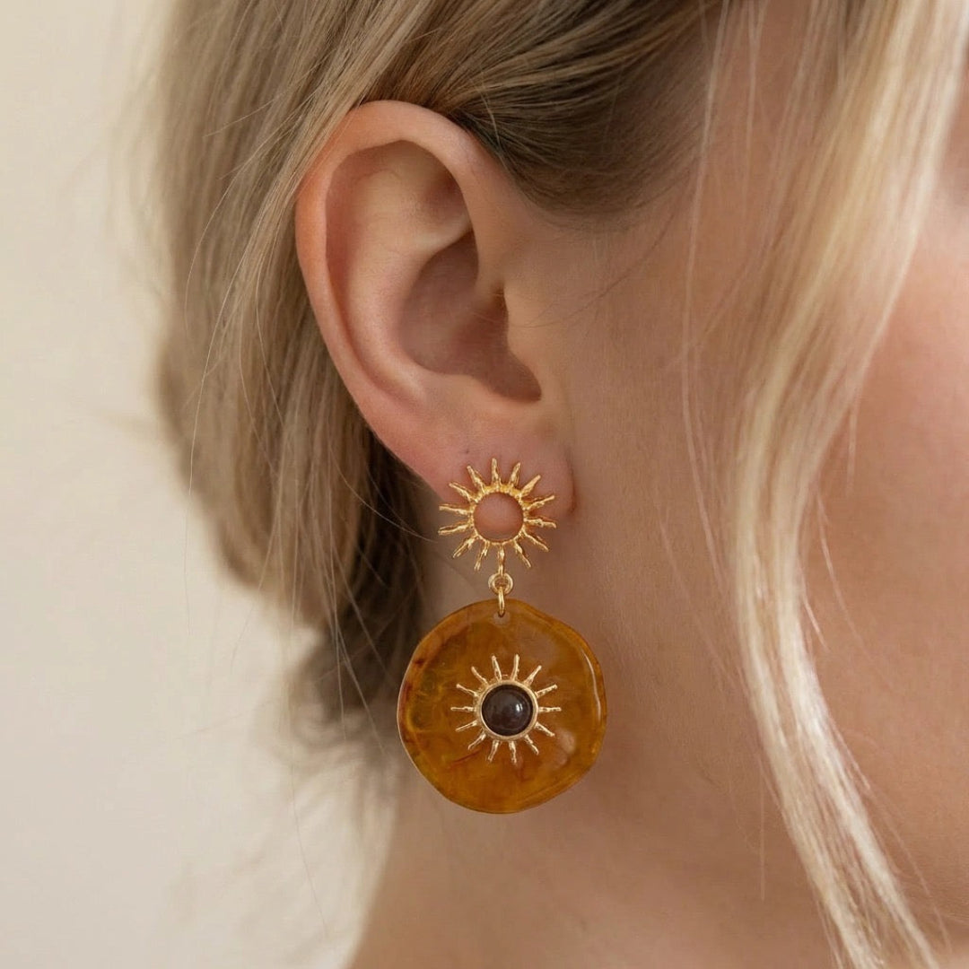 Close-up of a person wearing a sun-shaped earring with a brown disc.