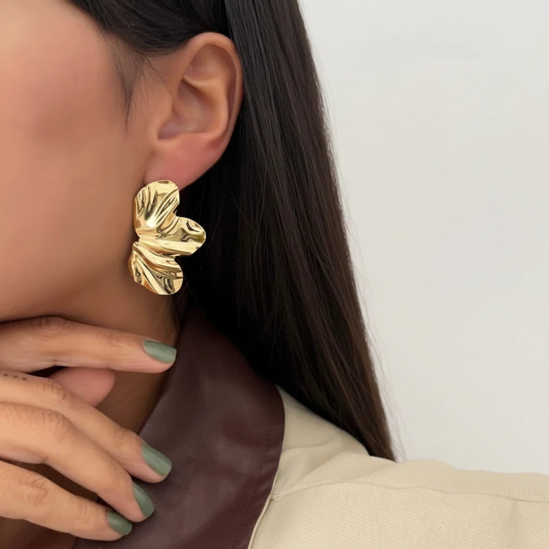 Gold leaf earrings being worn and held by a person with green nail polish.