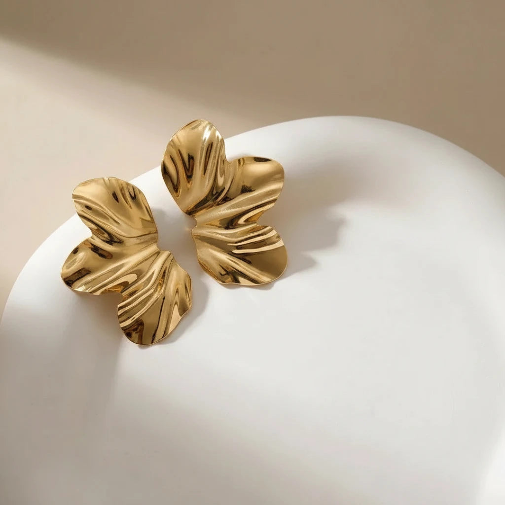 Pair of gold leaf-shaped earrings on a white surface with a beige background